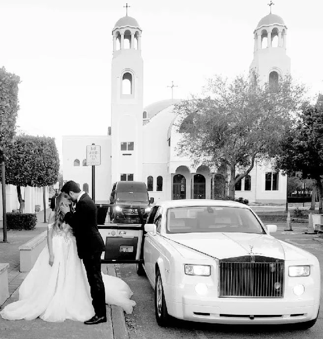 groom and bride kissing out of pearl white rolls royce phantom wedding car on wedding day.